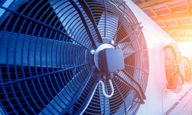 Close-up of large industrial fans mounted on an HVAC or cooling unit, with warm sunlight glowing in the background.