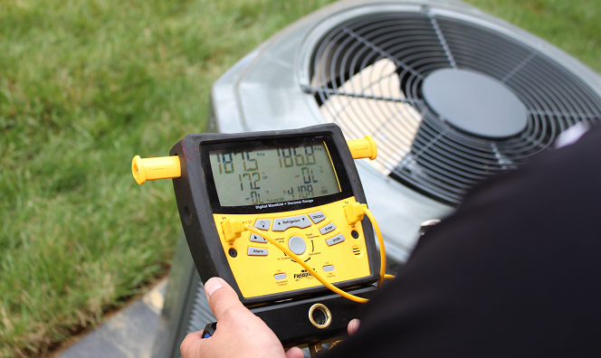 HVAC technician holding a digital manifold gauge to measure refrigerant pressure on an outdoor air conditioning unit.